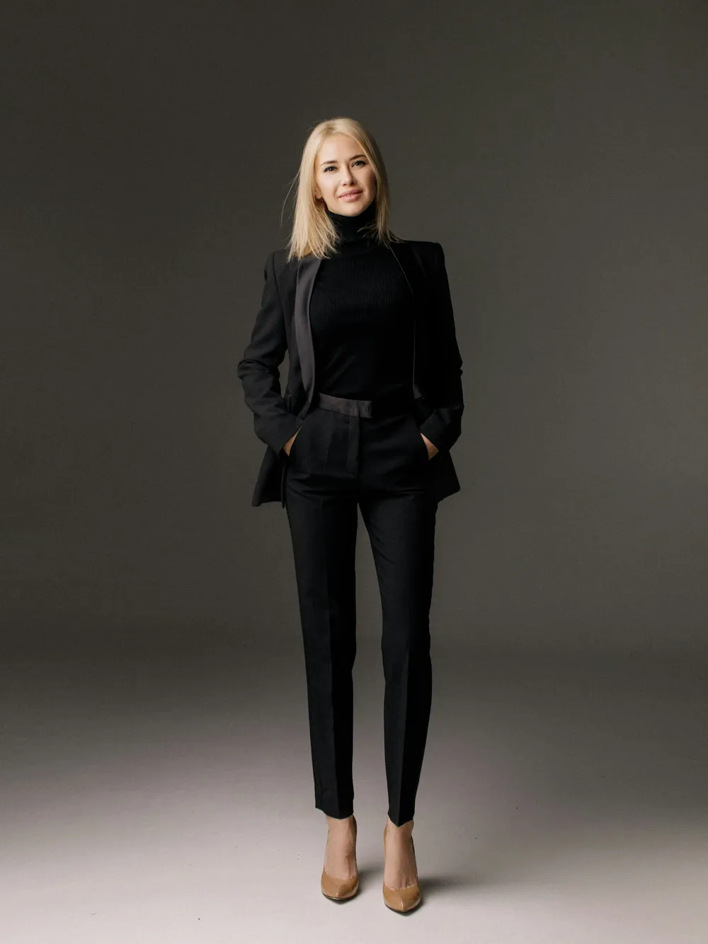 A businesswoman in a black suit standing against a gray studio backdrop