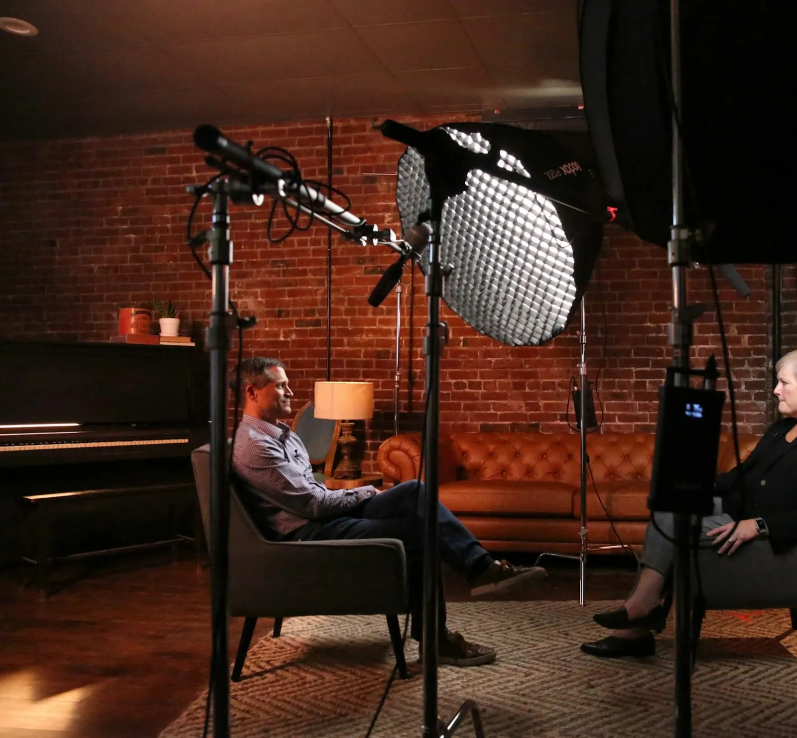A broadcast interview set with softbox lighting and a boom microphone, two people seated facing each other